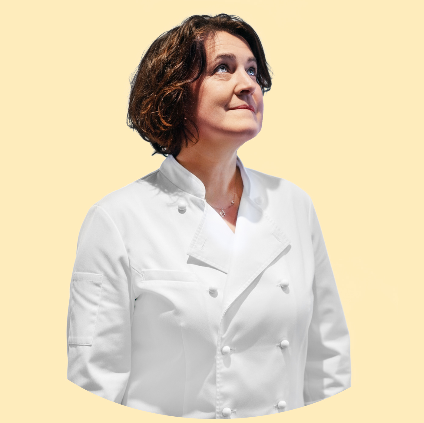 Woman with short brown hair wearing a white chef's jacket looking upward against a pale yellow background.